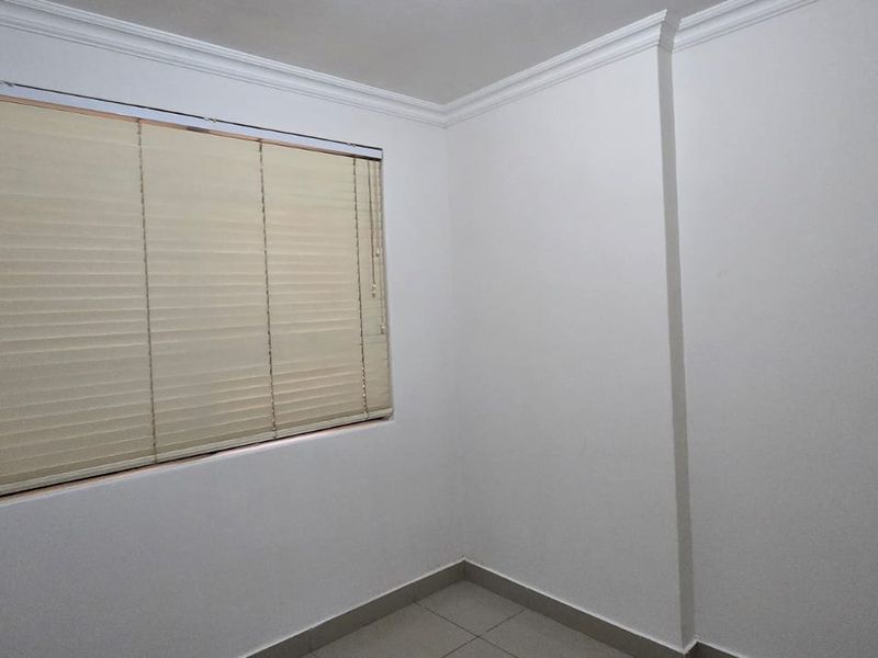A clean, empty bedroom featuring neutral tiled flooring, crown molding, and fitted venetian blinds, offering a blank canvas for personalization.