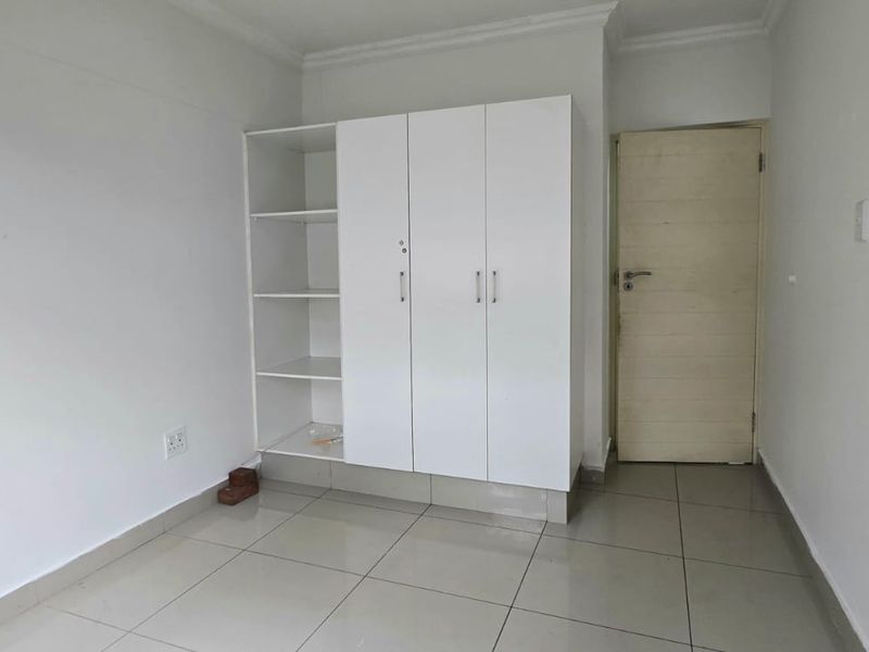 A clean, empty bedroom featuring neutral tiled flooring and a white built-in wardrobe with integrated shelving.