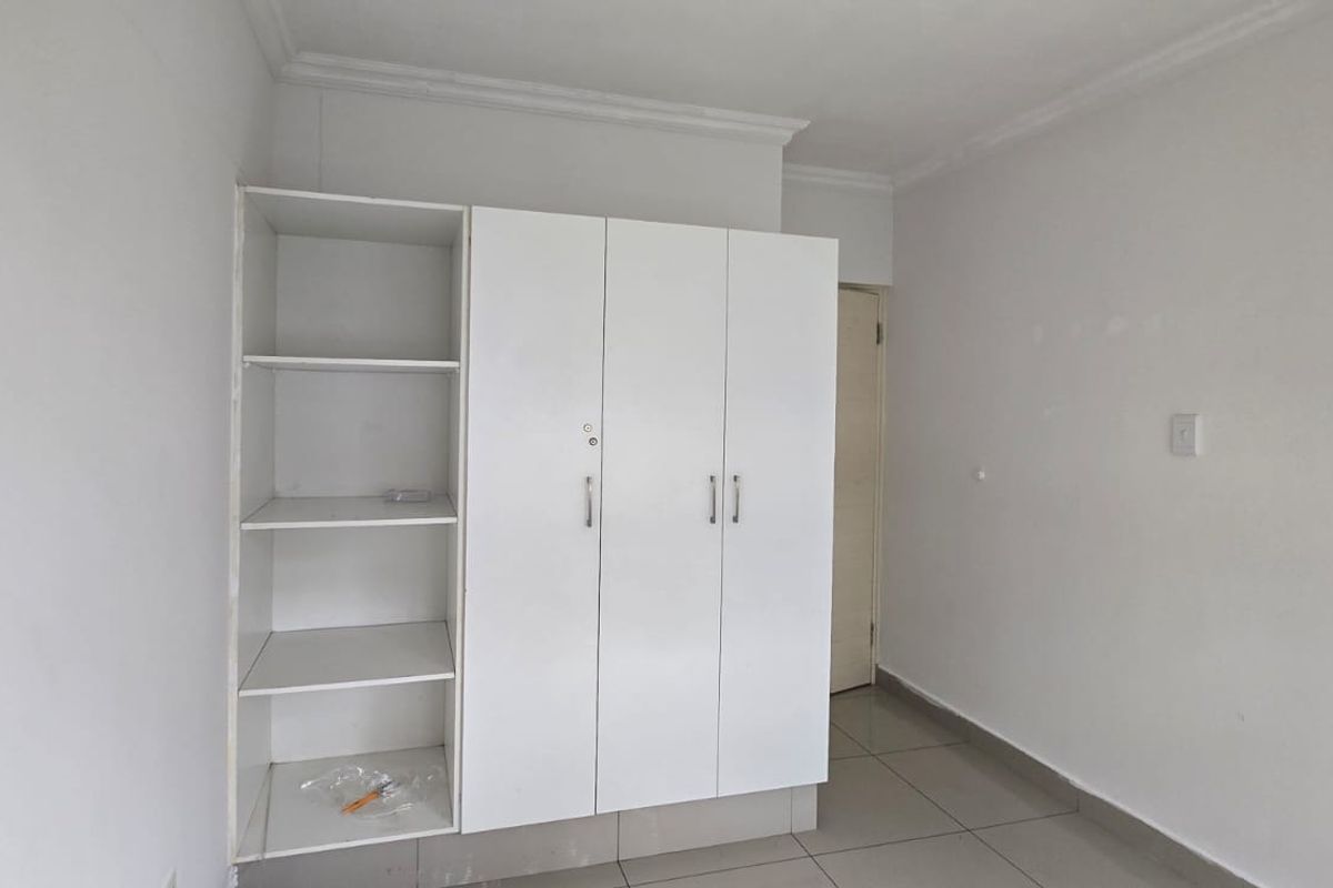 A clean, empty bedroom featuring neutral tiled flooring and a white built-in wardrobe with integrated shelving.