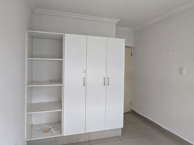 A clean, empty bedroom featuring neutral tiled flooring and a white built-in wardrobe with integrated shelving.