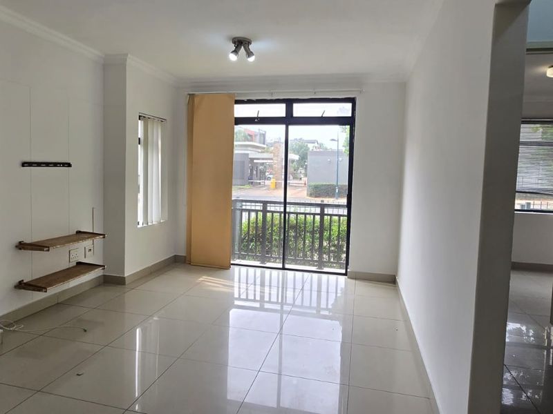 A bright, empty living room featuring neutral tiled flooring, clean white walls, and a sliding glass door providing access to a balcony.