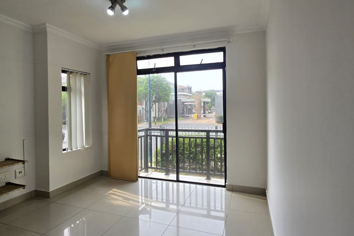 An empty living room featuring tiled flooring, wall-mounted shelving, and a sliding glass door leading to a balcony with exterior views.
