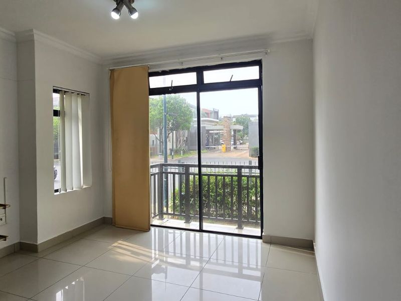An empty living room featuring tiled flooring, wall-mounted shelving, and a sliding glass door leading to a balcony with exterior views.