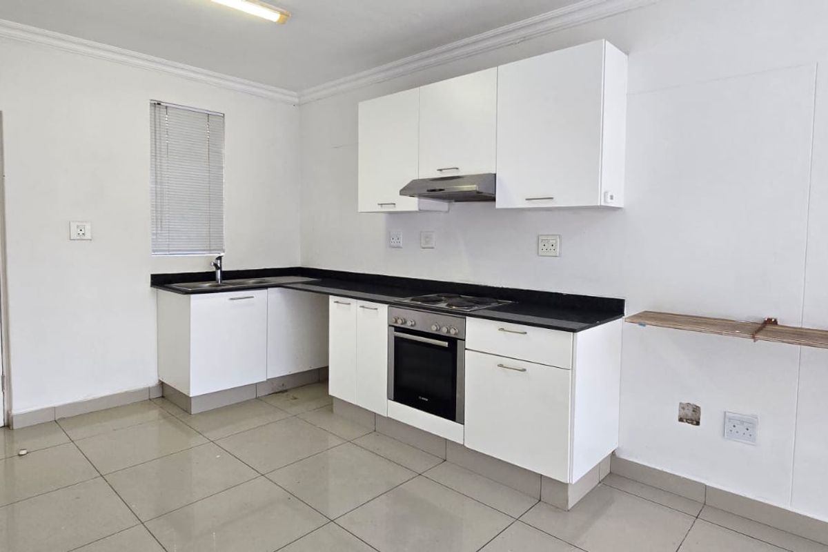 A functional kitchen featuring white cabinetry, black granite countertops, built-in oven and hob, and tiled flooring in a clean, minimalist space.
