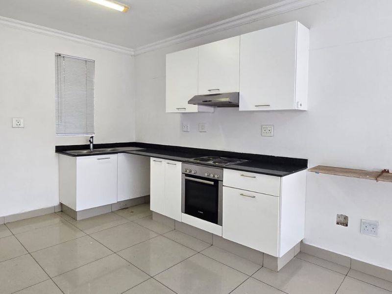 A functional kitchen featuring white cabinetry, black granite countertops, built-in oven and hob, and tiled flooring in a clean, minimalist space.
