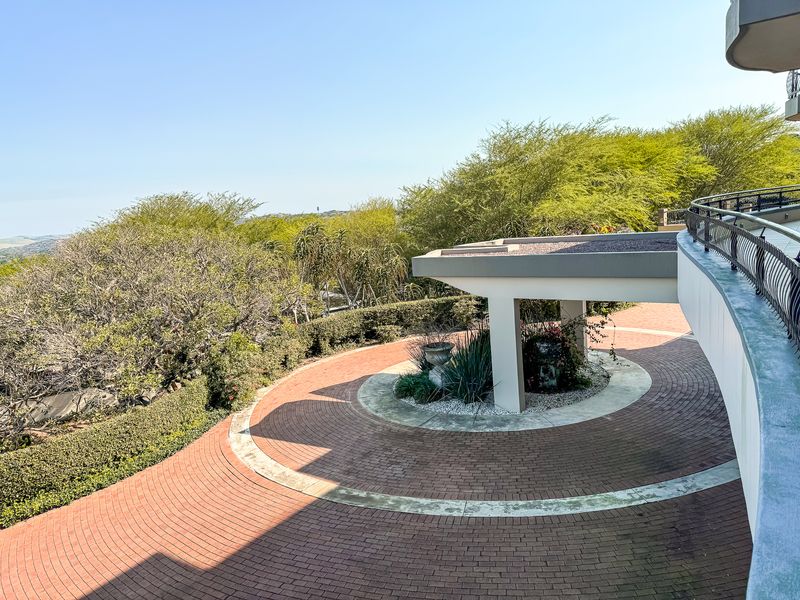 Elevated view of a circular brick paved driveway featuring a covered porte-cochere and surrounding landscaped garden area.