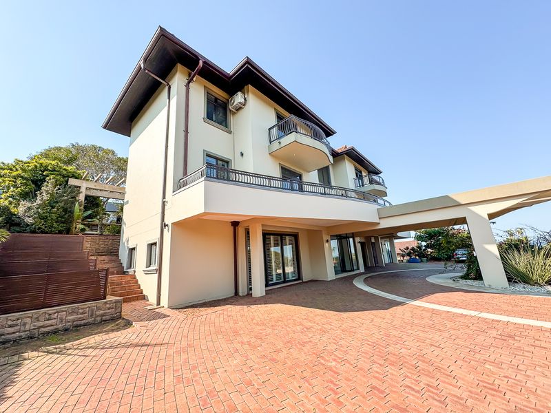 A multi-story residential property featuring a brick-paved driveway, covered porte-cochere, and upper-level balconies with metal railings.