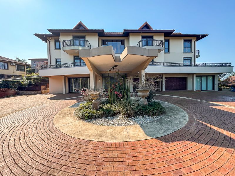 Grand multi-story residence featuring a prominent porte-cochere, circular paved driveway, and multiple balconies with wrought iron railings.