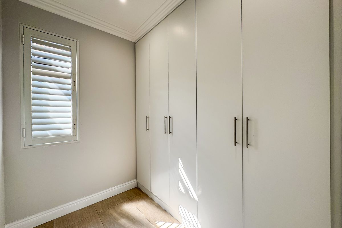 A clean, modern bedroom featuring floor-to-ceiling built-in cupboards, tiled flooring, and plantation shutters, offering a bright and well-maintained living space.