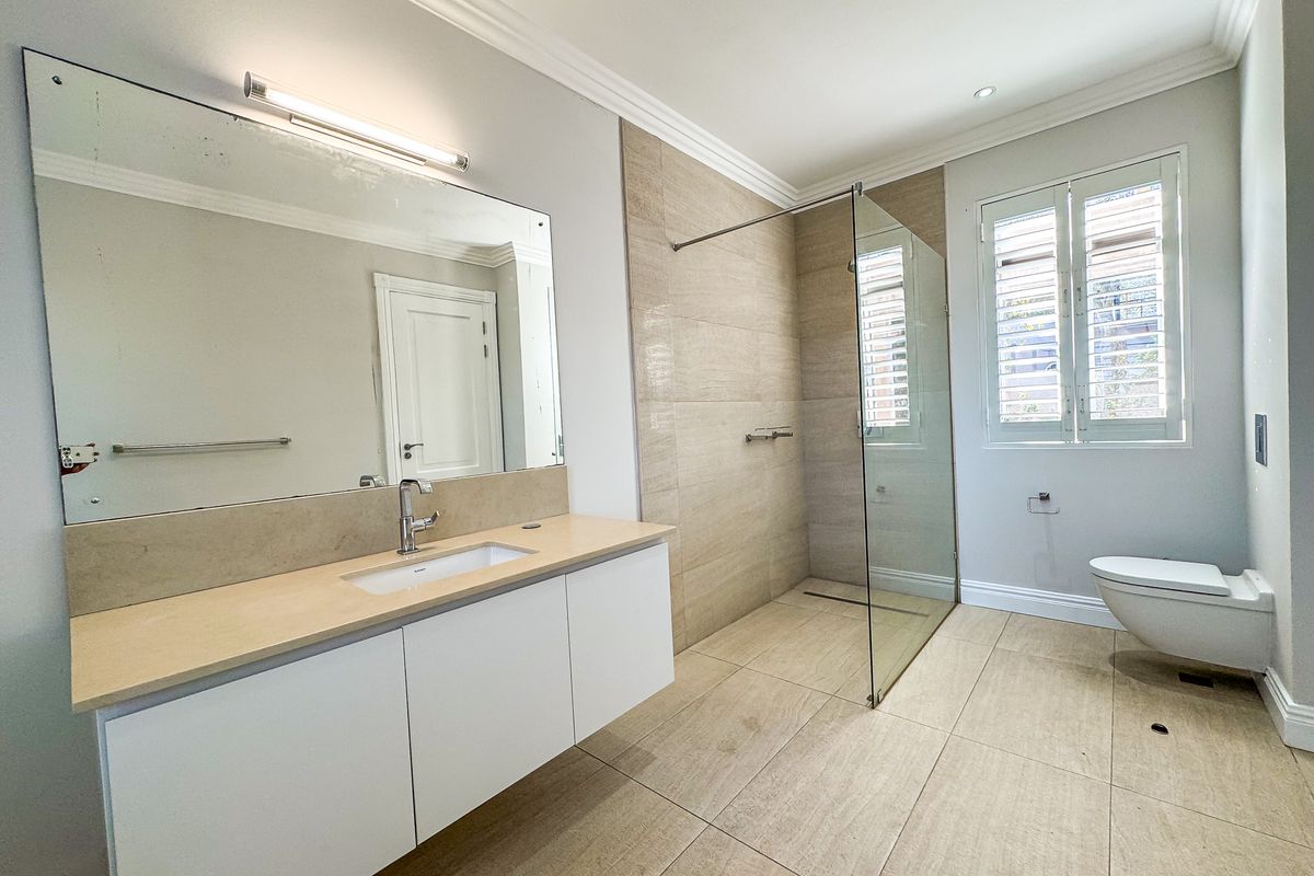 Modern bathroom featuring a wall-mounted vanity, walk-in shower with glass screen, wall-hung toilet, and neutral floor-to-ceiling tiling.