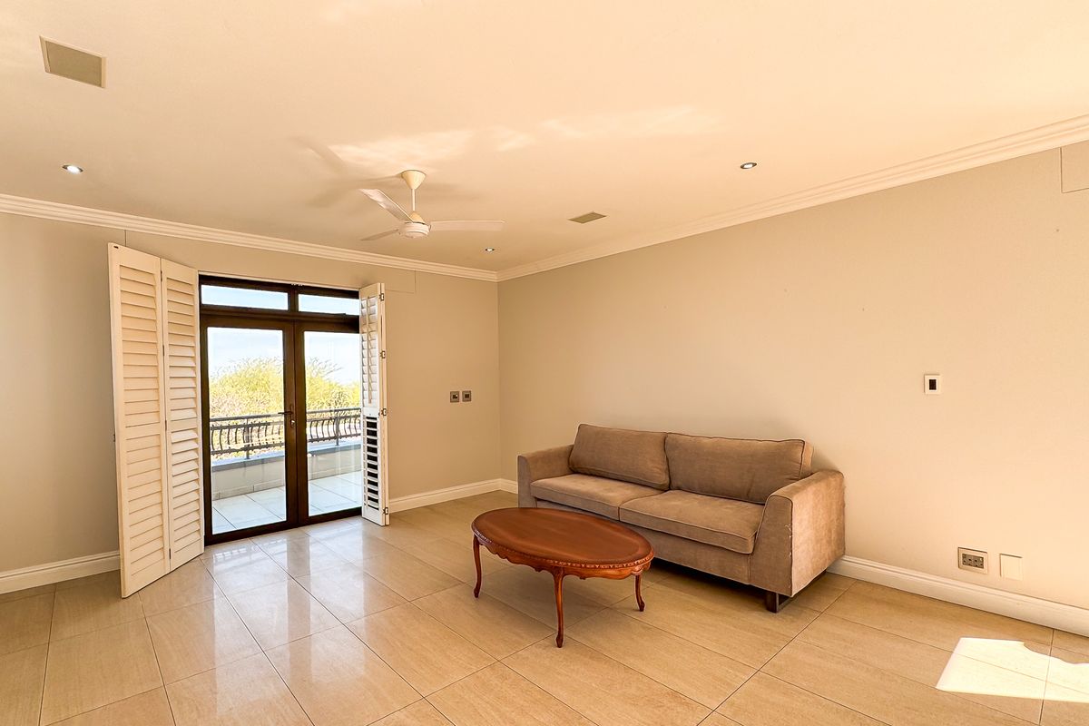 Spacious living room featuring large format floor tiles, recessed lighting, a ceiling fan, and double doors opening to a balcony with plantation shutters.