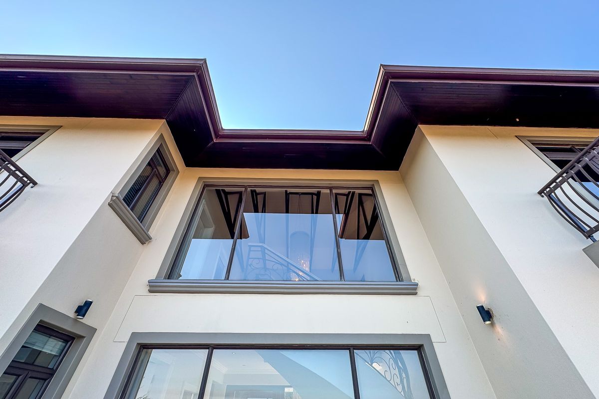 A low-angle view of the rear facade featuring large glass windows, dark timber eaves, and wrought iron balcony railings.