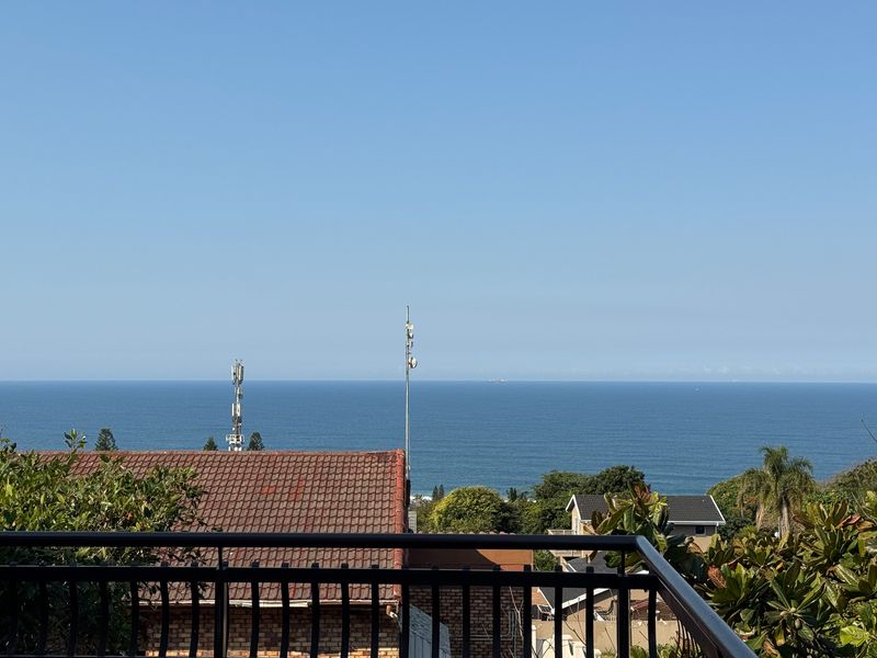 An elevated view overlooking the ocean, featuring a clear horizon line and surrounding residential rooftops.