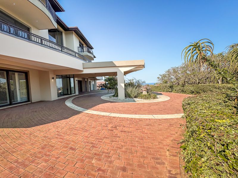A grand front entrance featuring a paved circular driveway, covered portico, and well-maintained landscaping leading to the main residence.