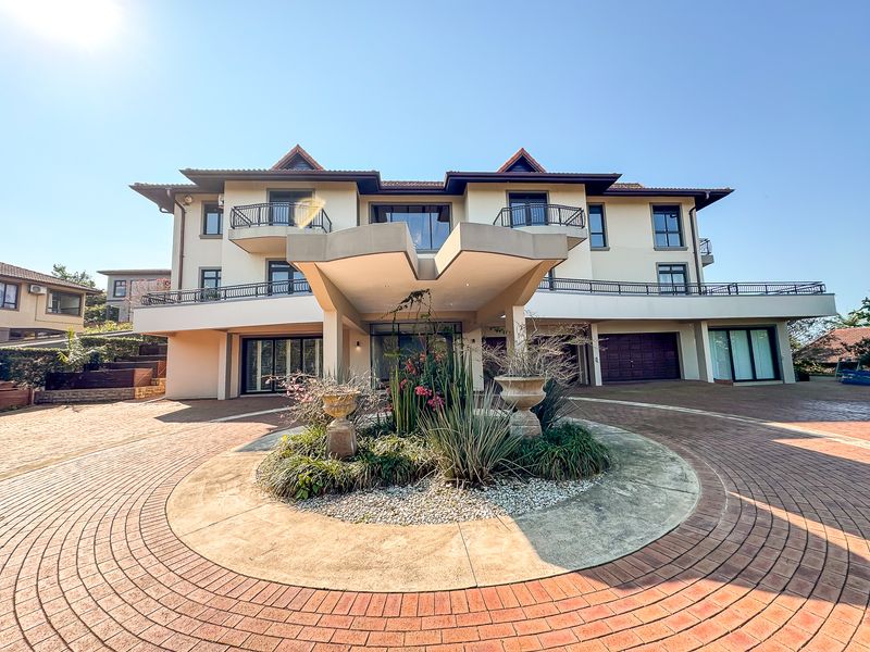 Grand front elevation featuring a circular brick paved driveway, prominent porte-cochere entrance, and multiple balconies with wrought iron railings.