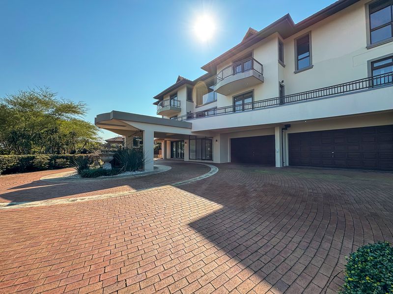 A grand multi-story residence featuring a circular brick paved driveway, covered entrance portico, and integrated double garage with balconies above.