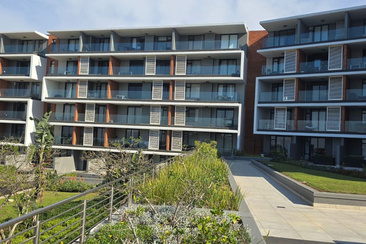 Modern apartment complex exterior featuring multi-level balconies with glass balustrades, louvre shutters, and well-maintained landscaped garden areas.