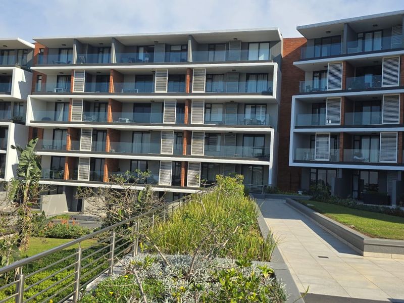 Modern apartment complex exterior featuring multi-level balconies with glass balustrades, louvre shutters, and well-maintained landscaped garden areas.