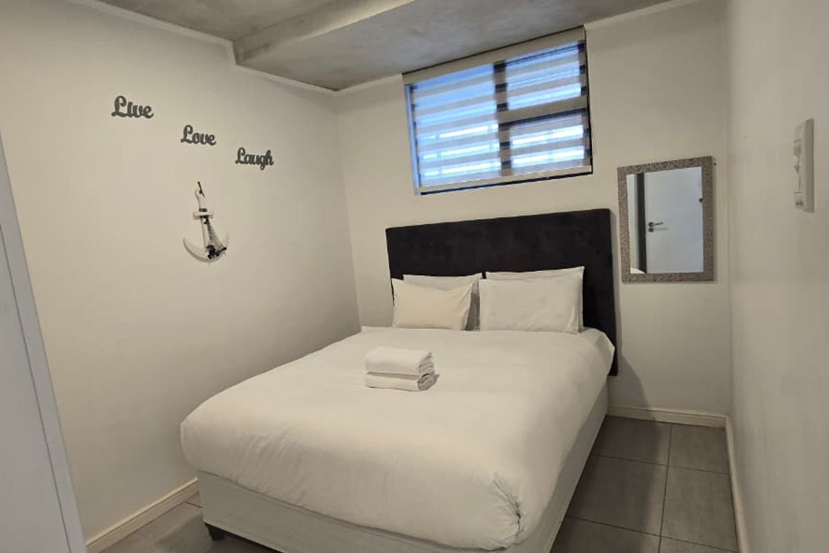 A compact bedroom featuring tiled flooring, a recessed ceiling detail, and a window fitted with horizontal blinds.