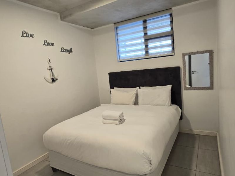 A compact bedroom featuring tiled flooring, a recessed ceiling detail, and a window fitted with horizontal blinds.