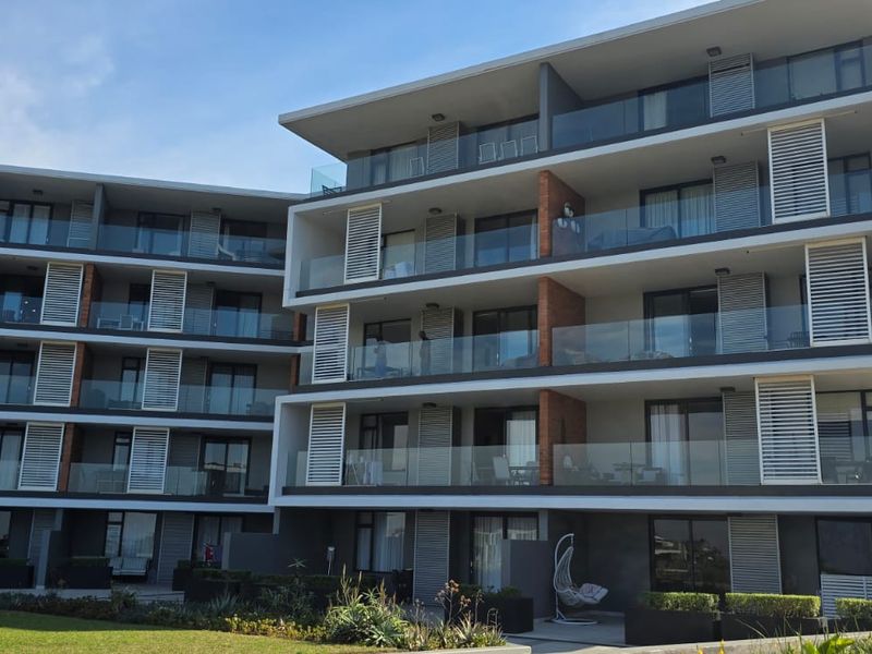 Modern multi-story apartment building featuring contemporary architecture with glass balustrades, private balconies, and integrated louvred shutters overlooking a landscaped garden area.