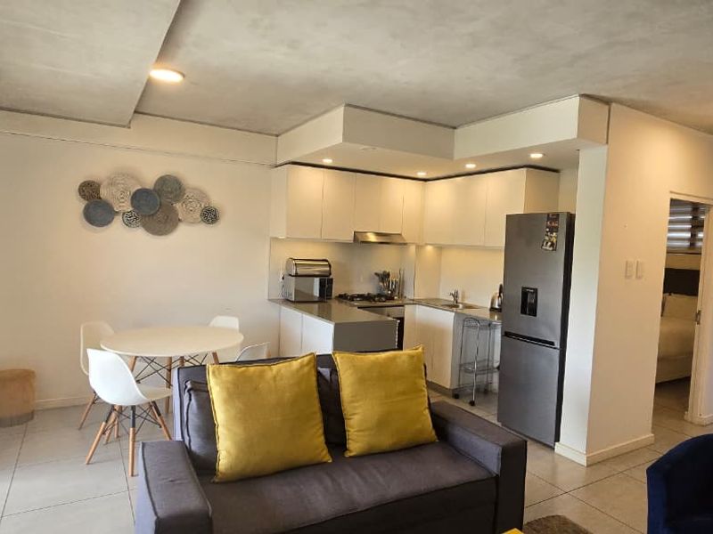 An open-plan living and kitchen area featuring modern cabinetry, tiled floors, and direct access to a balcony through sliding glass doors.