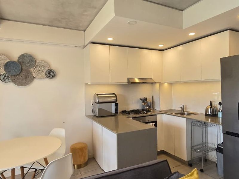 Modern open-plan kitchen featuring sleek white cabinetry, stone countertops, integrated gas hob, and recessed lighting, seamlessly flowing into the dining area.