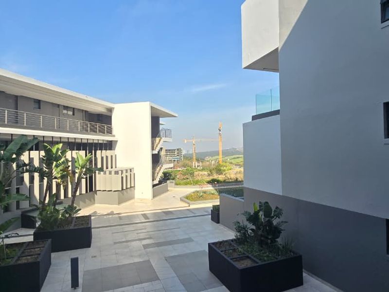 A modern apartment complex courtyard featuring paved walkways, built-in planters, and contemporary architectural design with glass balustrades.