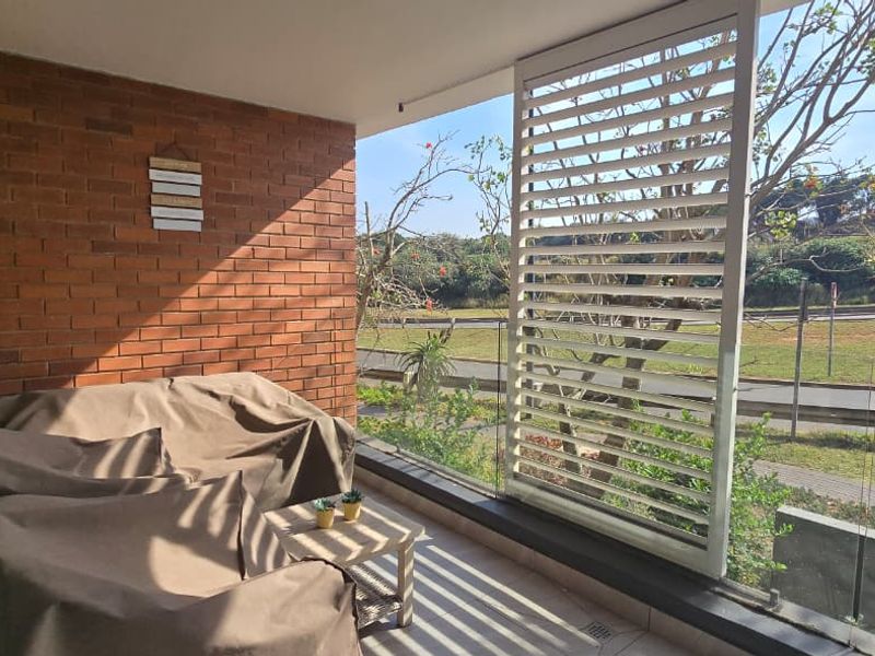 A covered balcony featuring an exposed brick wall, glass balustrade, and an adjustable privacy screen, offering a pleasant outdoor space.