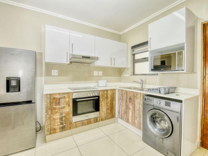 Modern kitchen featuring white and wood-grain cabinetry, integrated appliances, tiled backsplash, and sleek tiled flooring.
