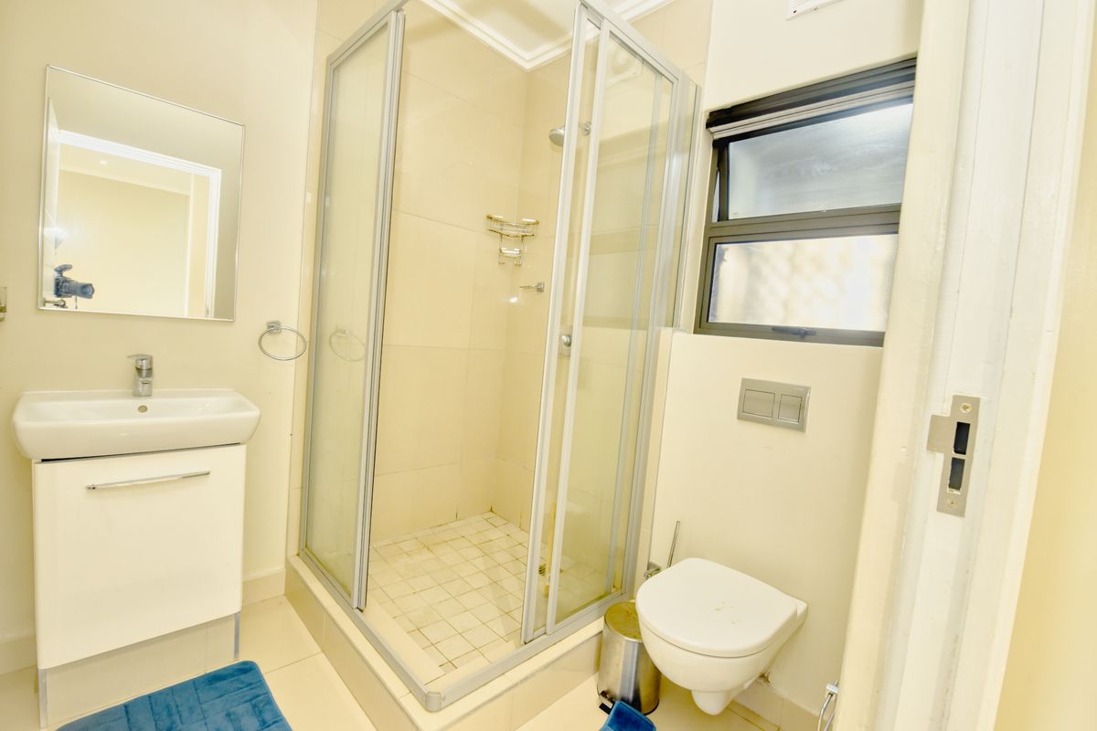 A clean, functional bathroom featuring a glass shower enclosure, wall-mounted toilet, and a modern vanity basin with a mirror.