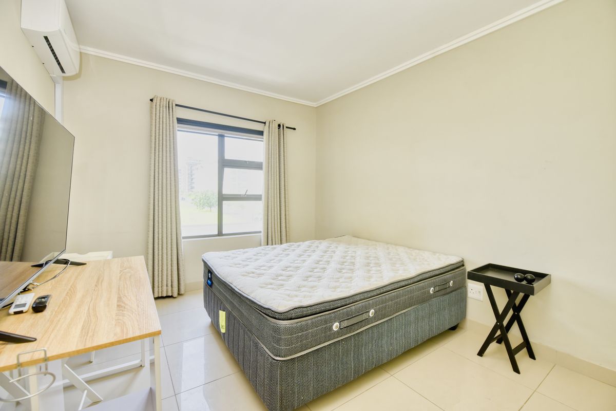 A well-lit bedroom featuring tiled flooring, an installed air conditioning unit, and large aluminium-framed windows with neutral wall finishes.