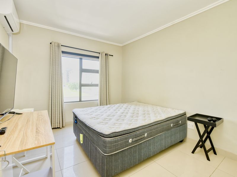 A well-lit bedroom featuring tiled flooring, an installed air conditioning unit, and large aluminium-framed windows with neutral wall finishes.