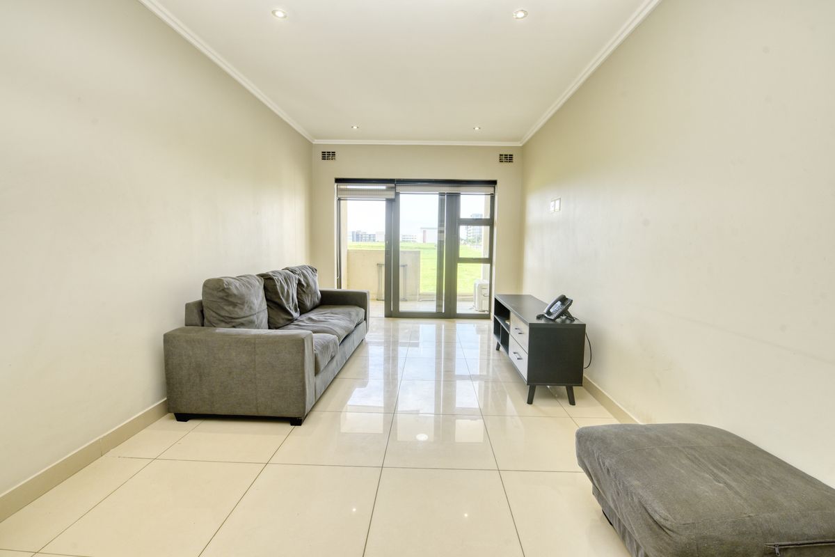 A bright living room featuring polished tiled flooring, recessed downlighting, and a large sliding glass door providing access to the balcony.