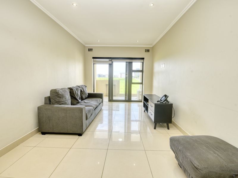 A bright living room featuring polished tiled flooring, recessed downlighting, and a large sliding glass door providing access to the balcony.