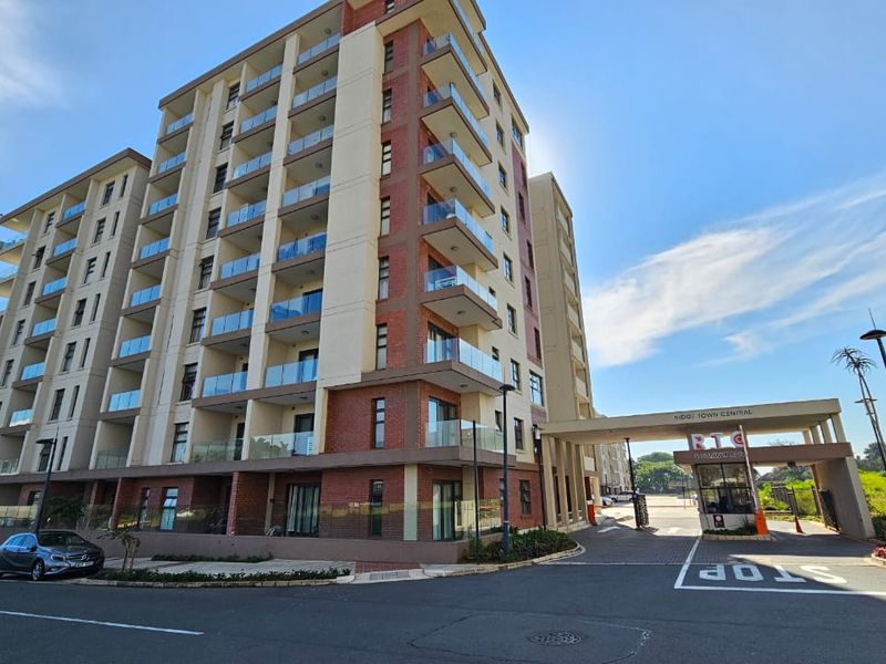 Modern multi-story apartment complex featuring brick and plaster facade, glass-fronted balconies, and a secure gated entrance with a guardhouse.