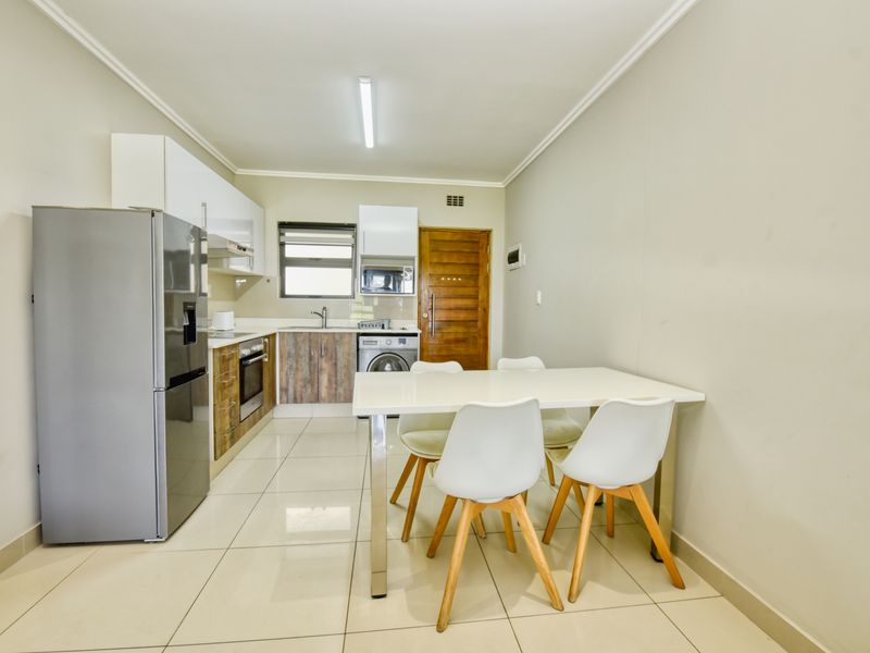 An open-plan kitchen and dining area featuring modern cabinetry, built-in appliances, and neutral tiled flooring throughout.