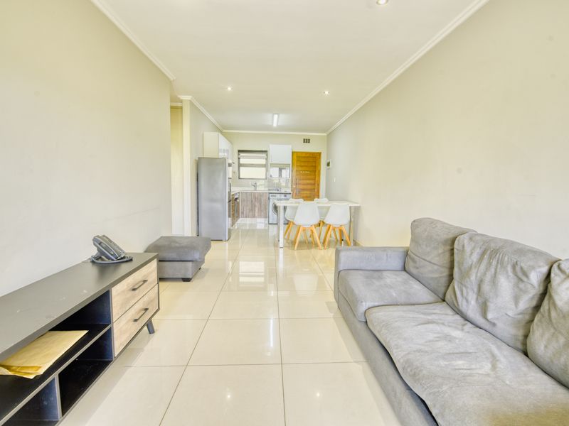 Open-plan living and kitchen area featuring neutral tiled flooring, recessed lighting, and a functional kitchen layout with built-in cabinetry and appliances.
