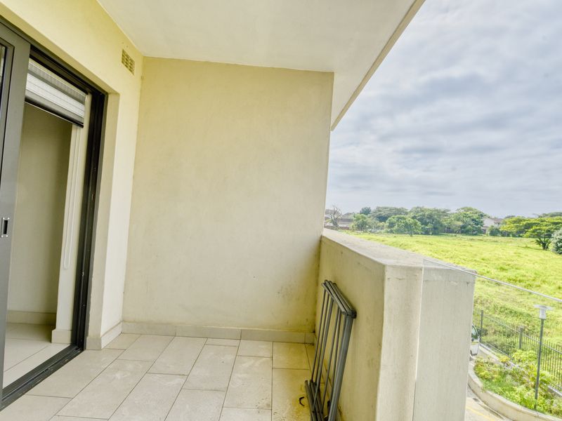 A private balcony featuring tiled flooring and a solid balustrade, offering an open outlook over the surrounding green landscape.