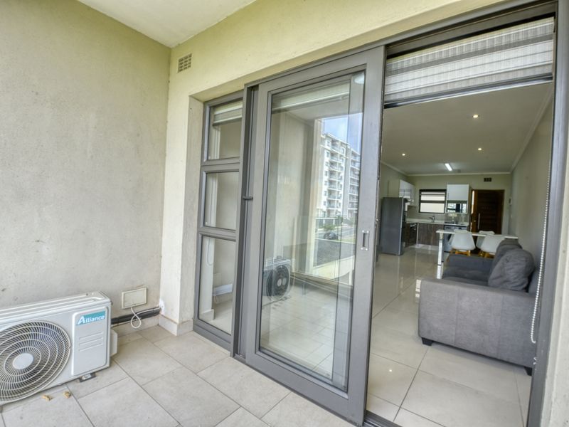 A covered balcony featuring tiled flooring and an external air conditioning unit, providing seamless access to the open-plan interior living space.