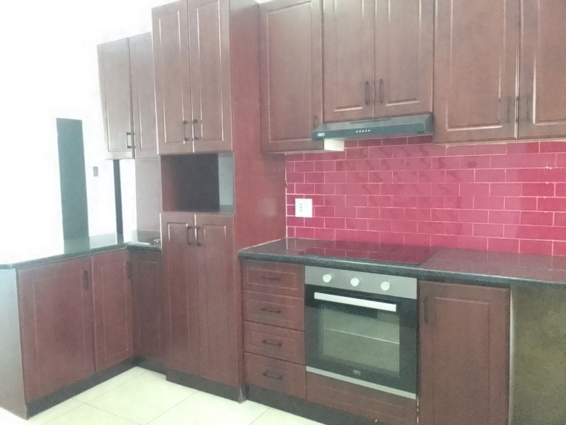 A functional kitchen featuring dark wood cabinetry, granite countertops, a red tiled backsplash, and built-in oven and hob appliances.