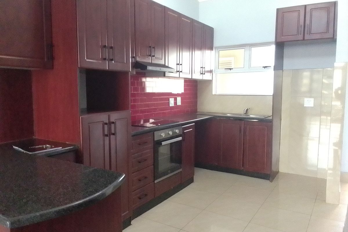 A clean, functional kitchen featuring dark wood cabinetry, granite countertops, a red subway tile backsplash, and integrated appliances including an oven and hob.