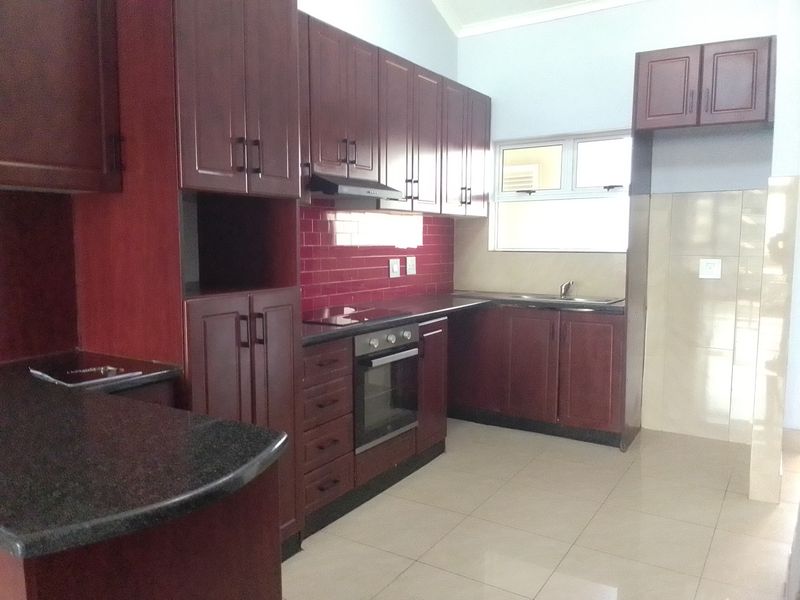A clean, functional kitchen featuring dark wood cabinetry, granite countertops, a red subway tile backsplash, and integrated appliances including an oven and hob.