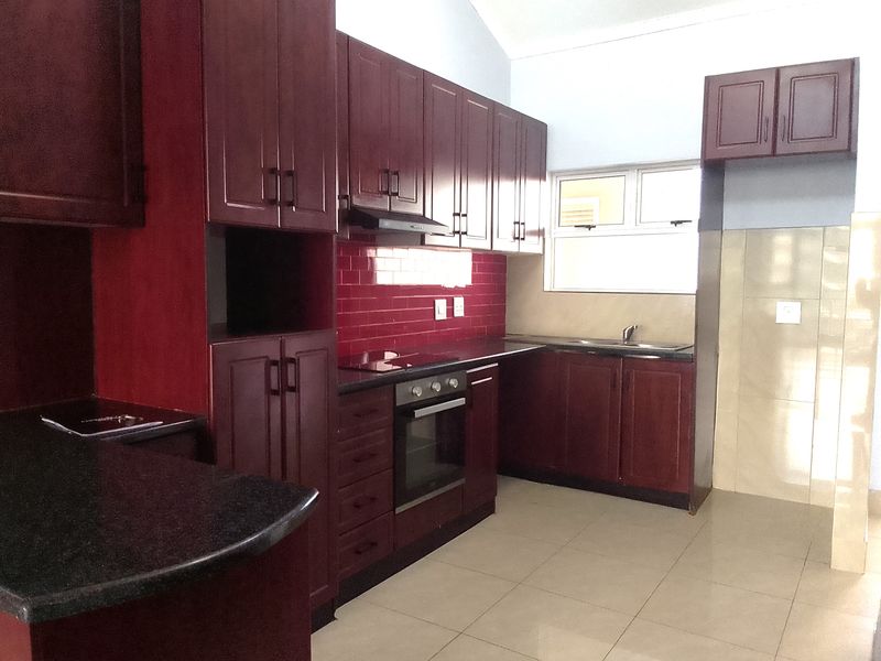 A functional kitchen featuring dark wood cabinetry, granite countertops, a red subway tile backsplash, and built-in appliances including an oven and hob.
