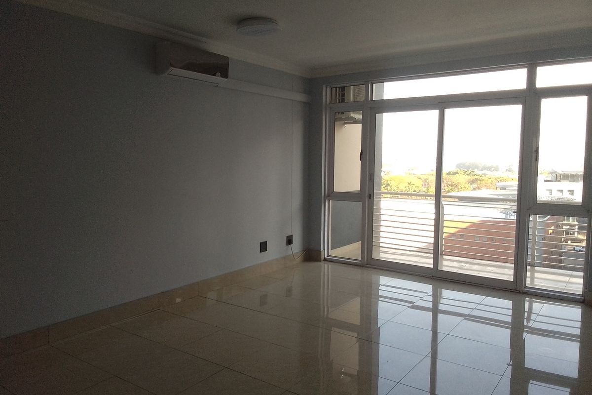 A bright, empty living room featuring polished tiled floors, a wall-mounted air conditioning unit, and large sliding glass doors leading to a balcony.