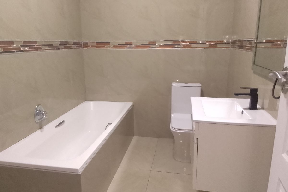 A clean, modern bathroom featuring a built-in bathtub, wall-mounted toilet, and a vanity cabinet with a contemporary basin and mixer tap.