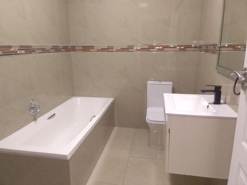 A clean, modern bathroom featuring a built-in bathtub, wall-mounted toilet, and a vanity cabinet with a contemporary basin and mixer tap.