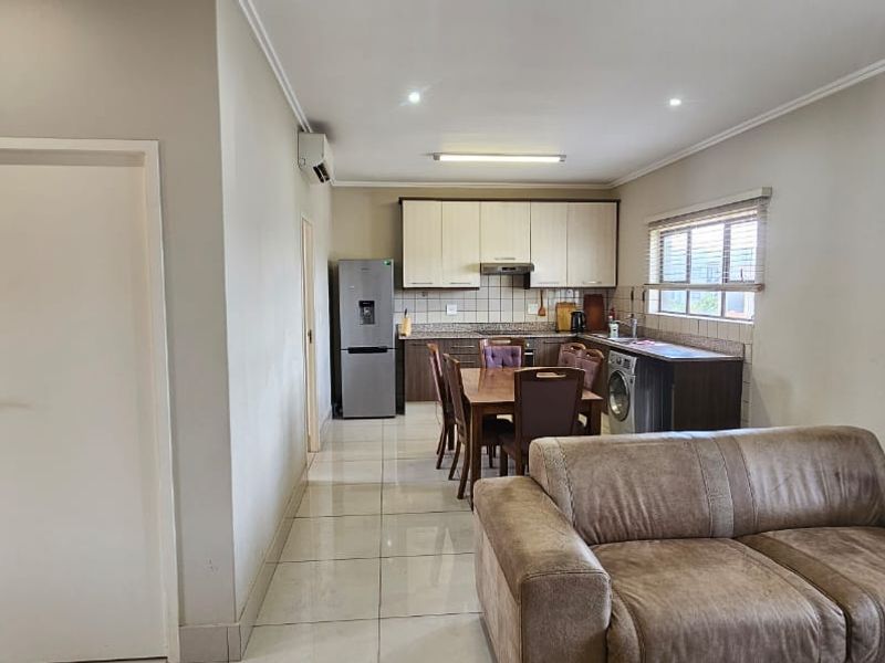An open-plan living and kitchen area featuring tiled flooring, neutral walls, and functional built-in cabinetry with integrated appliances.