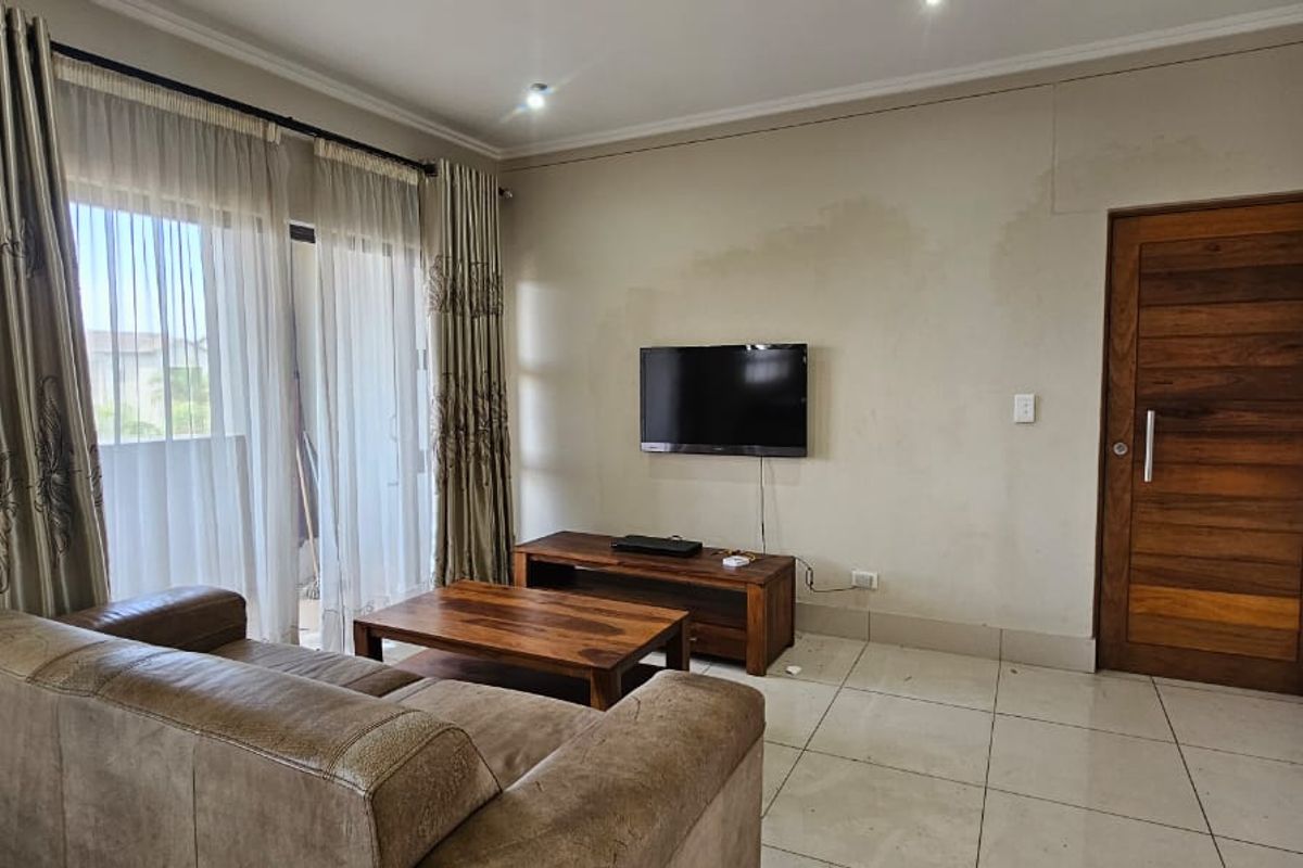 Living room featuring tiled flooring, a sliding glass door to the balcony, and a wooden door. Note visible water staining on the wall.