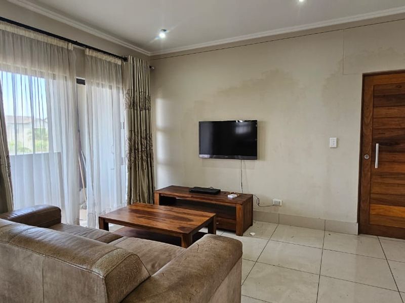 Living room featuring tiled flooring, a sliding glass door to the balcony, and a wooden door. Note visible water staining on the wall.